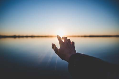 people landscape photography of person's hand in front of sun finger