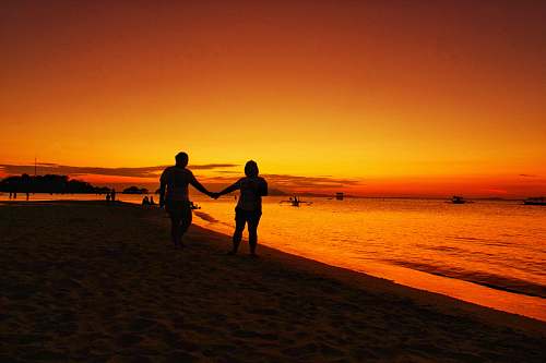 human man and woman walking hand in hand in beach at sunset person