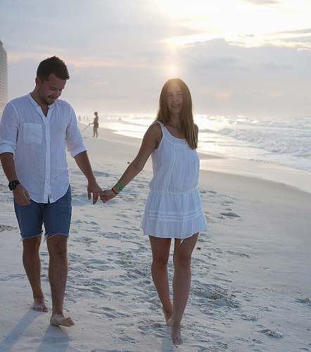 person man and woman walking on seashore holding hands