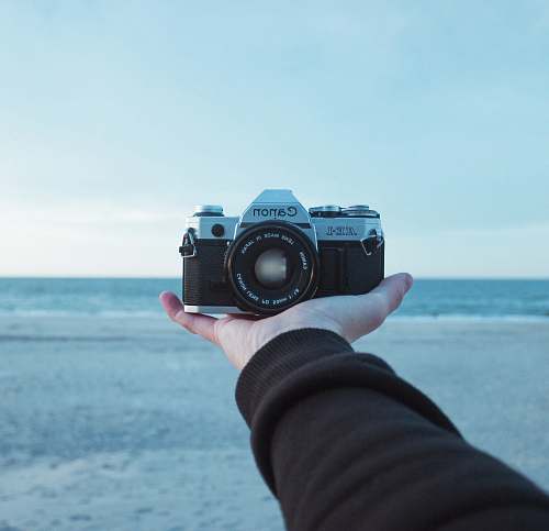 camera person holding black and gray Canon AE-1 bridge camera electronics
