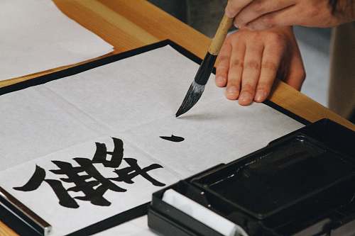 calligraphy person holding black paint brush while painting black text on white paper japan