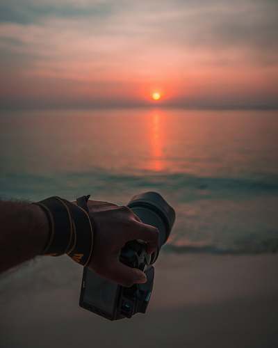 nature person holding camera near sea during golden hour outdoors
