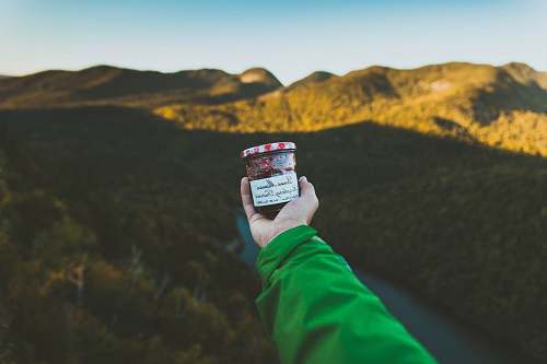 hiking person holding clear glass jar with cap near mountain jar