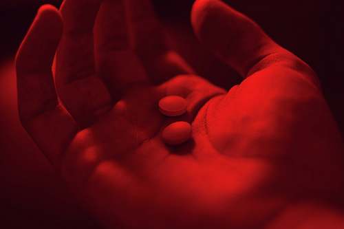 finger person holding two medicine pills red