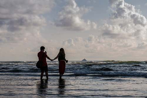 person silhouette of two people holding hands at seashore human
