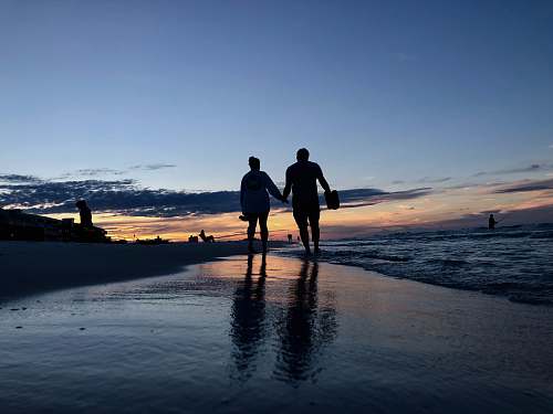 person silhouette photography of two people walking on seashore human