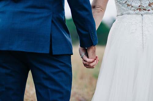 human woman wearing white wedding dress and man wearing blue suit holding hands during daytime holding hands