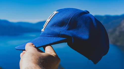 blue person holding blue fitted cap mountain