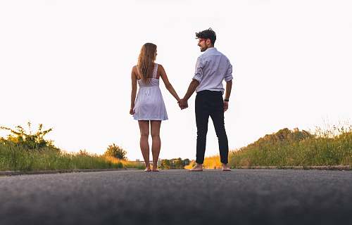 person man and woman standing holding hands together while walking on road holding hands