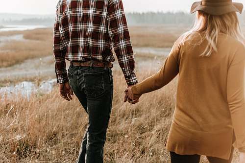 person man and woman walking along grass field while holding hands holding hands