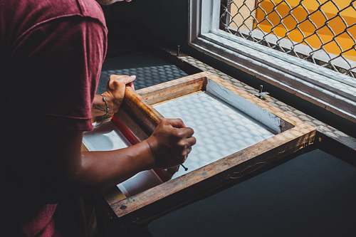 person man holding printing screen near white window people