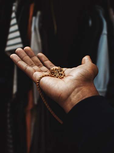 person person holding chain gold-colored necklace finger