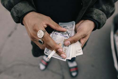 person person holding dollar banknotes while pinning cigarette stick people