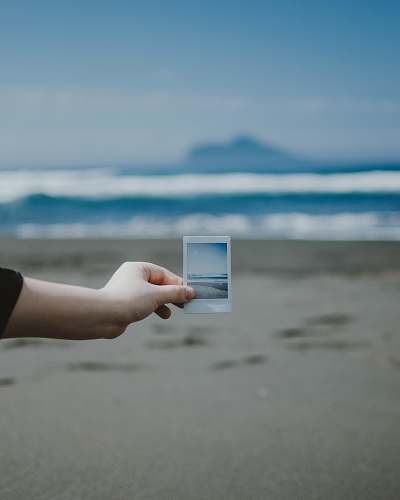 person person holds photo of ocean at the beach finger