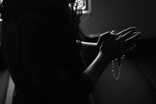 person silhouette of woman holding rosary while praying black-and-white