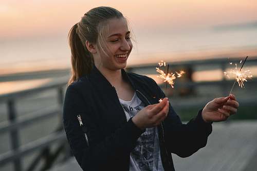 person woman wearing black zip-up jacket standing while holding lighted sparklers finger