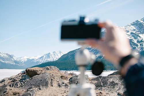 hand person holding camera distance with white mountains mountain