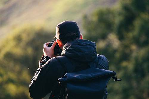 person man standing near mountain cliff while taking photo human