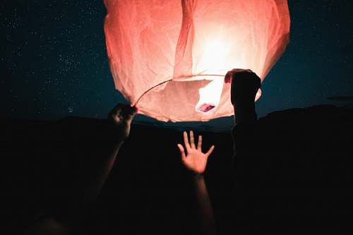human three human hand about to catch and hold sky lantern at night time person