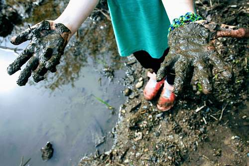 finger child in green top with mud on hand hand