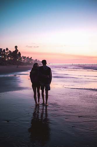 human couple standing beside body of water during daytime hand