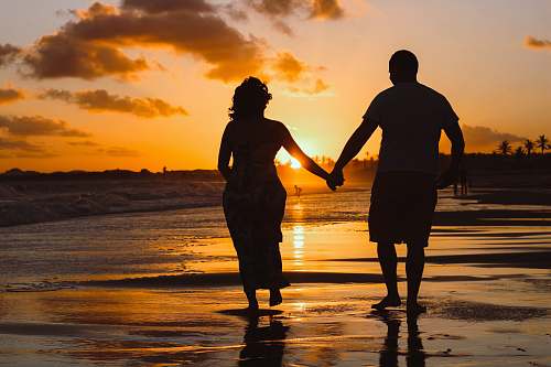 human couple standing on body of water during golden hour hand