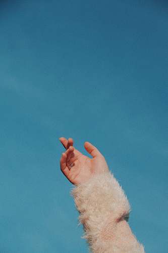 finger human hand wearing beige fur sleeved under blue sky blue