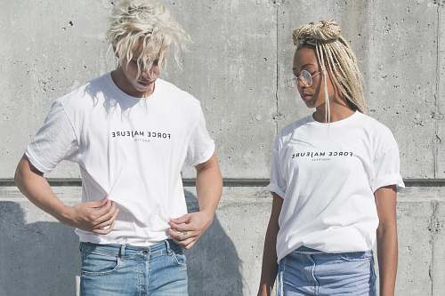 human man and woman in white-and-gray force majeure-printed crew-neck t-shirts standing near gray concrete wall people