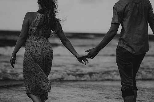 human man and woman walking on beach black-and-white