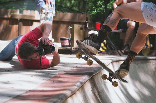 human man lying on floor while taking picture of person doing skate trick on ramp photographer