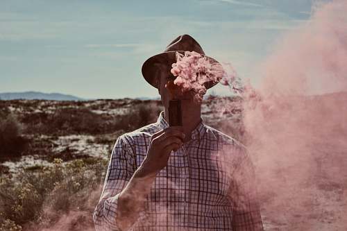 human man standing on open field holding device with smoke during daytime people