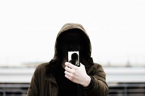 human man wearing black hooded jacket and holding smartphone white taking close-up selfie people
