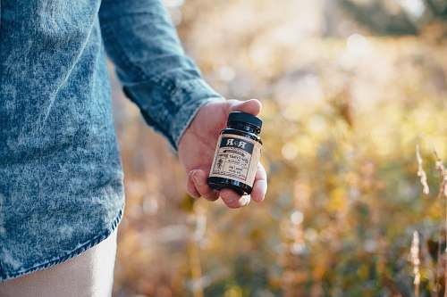 hemp person holding beige and black glass bottle human