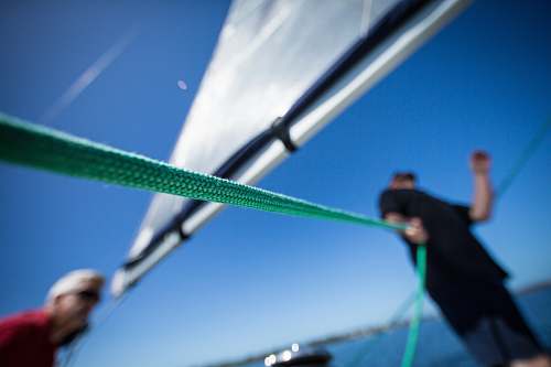 sailing person holding green rope near boat sail human