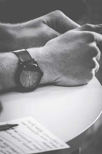 black-and-white person wearing black watch with hand on table wristwatch