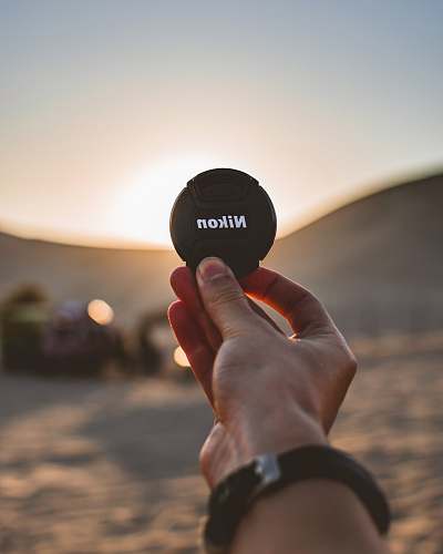human shallow focus photo of black Nikon camera lens cover finger