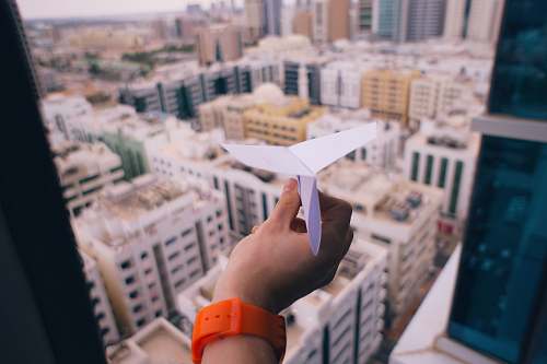city shallow focus photography of person holding paper plane building