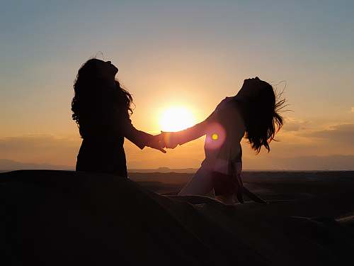 nature silhouette photo of two women holding each other hands outdoors