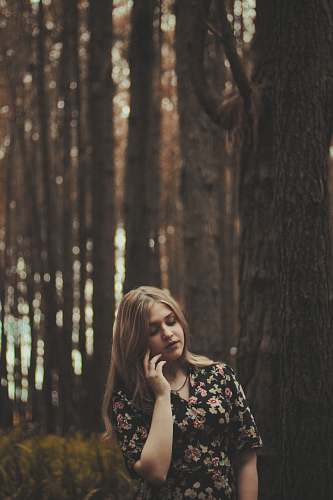 human standing woman beside gray tree while holding left cheek during daytime girl