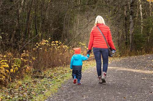 human woman and boy walking on road near bush during daytime holding hands