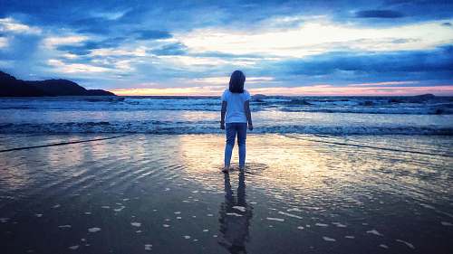 human woman in white shirt standing near beach during daytime standing