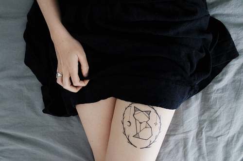 human woman lying on bed sowing cat dreamcatcher tattoo on right leg during daytime dress