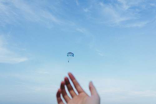 hand person riding parachute at daytime blue