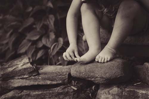 rocks depth photography of child sitting on rock beside plant kid