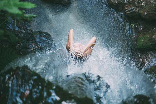 pool high-angle photography of woman bathing below waterfalls during daytime woman