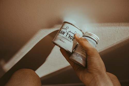hand person holding glass bottle and white soft wax can holding