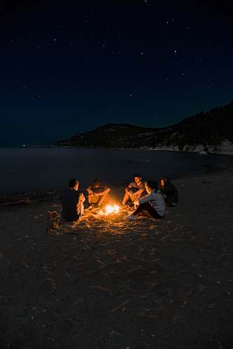 flame people sitting near campfire near seashore camping