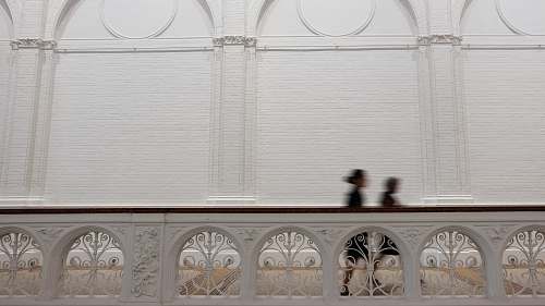 busy time-lapse photography of two person walking at hallway between concrete fence and wall fast