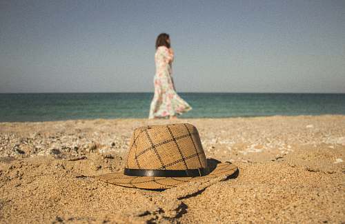 clothing woman walking near seashore and brown and gray hat on brown sand hat