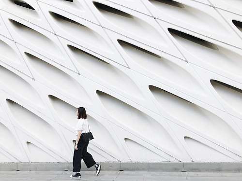 human woman wearing white top and black pants near wall person